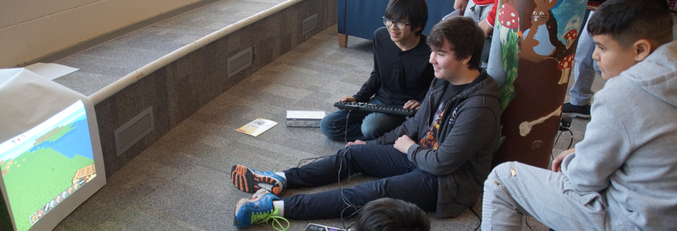 Male students sitting on carpet playing a coding game
