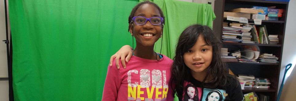 Two female students standing in front of a green screen